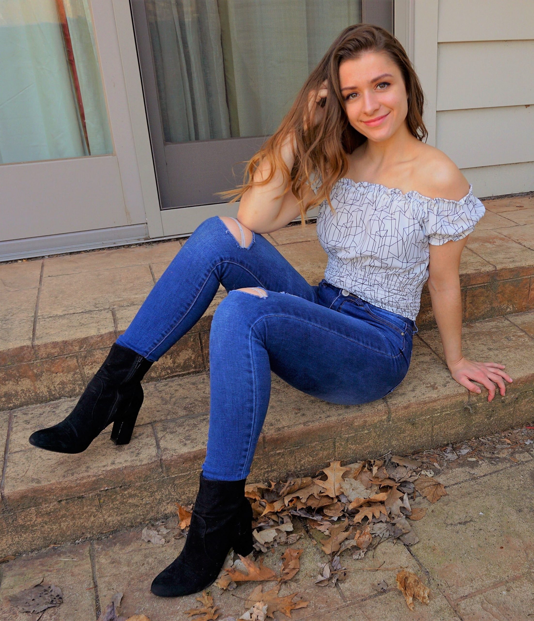 woman sitting on step and wearing off shoulder top and jeans